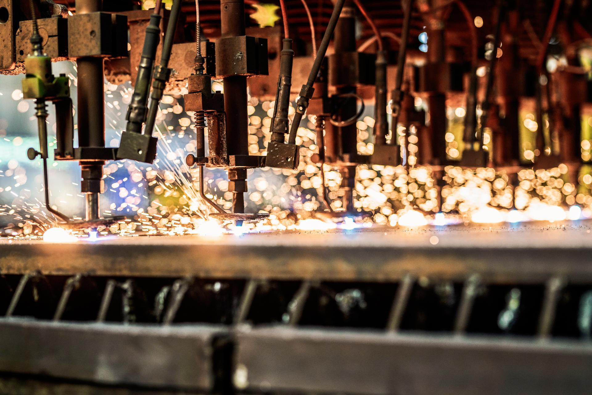 Nahaufnahme einer Reihe von industriellen Schneidbrennern, bei denen Funken sprühen, während sie Metall schneiden.