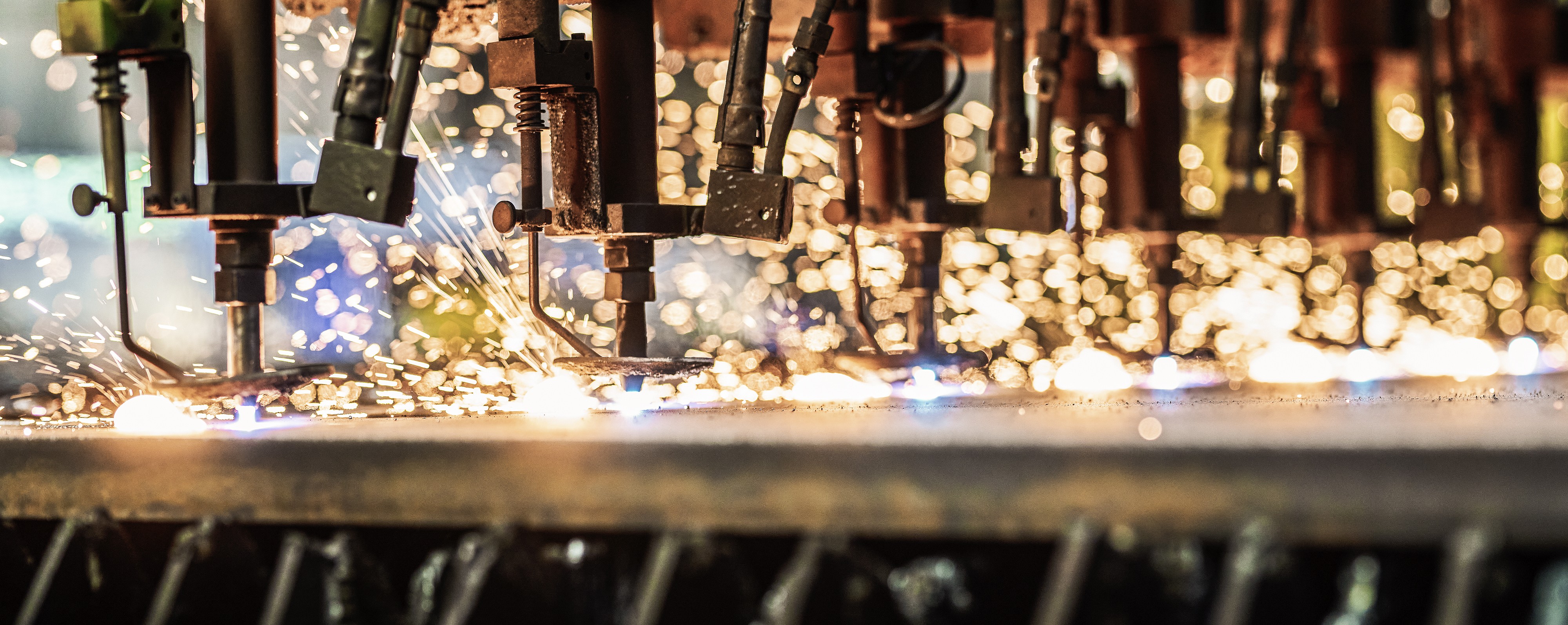 Nahaufnahme eines Metallbearbeitungsprozesses mit automatisierten Maschinen, bei dem Funken sprühen.